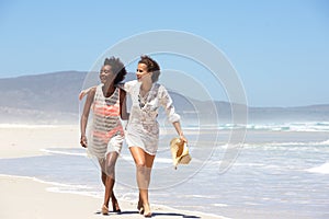 Two young women walking barefoot on beach