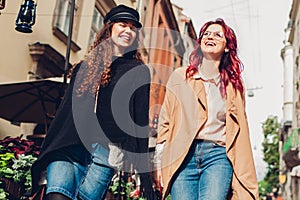 Two young women walking on city street laughing. Friends talking and having fun together