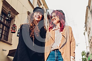 Two young women walking on city street laughing. Friends talking and having fun together