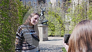 Two young women walking in the park among decorative plants and taking pictures with statues