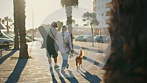 Two youngsters walking summer street with pet back view. Guy embracing woman