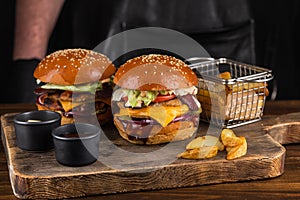 Two yummy big grilled burger with double meat cutlet and cheese on a wooden board ready to eat. Burger and fries