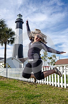 Tybee Island Light House in coastal Georgia. Blonde woman jumps in front of the lighthouse