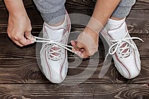 Tying Shoe laces girl sitting on the wooden floor. White sneakers on a dark wooden background.The view from the top