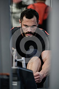 Tying shoes in sport gym by strong young caucasian man with beard during training break for relaxation