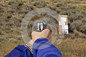 1911-type semi-automatic pistol in a two-hand hold aimed at a cardboard target on an outdoor range photo