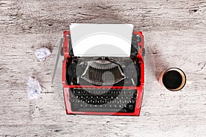 The typewriter is red with paper in it and on the table