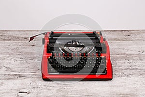 The typewriter is red with paper in it and on the table
