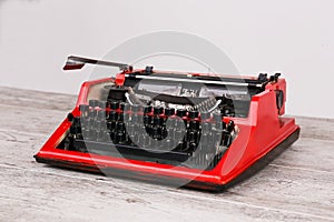 The typewriter is red with paper in it and on the table
