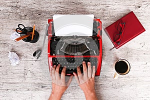 The typewriter is red with paper in it and on the table