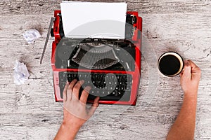 The typewriter is red with paper in it and on the table