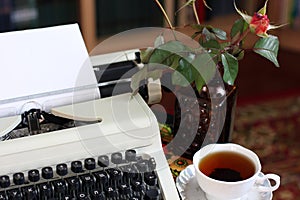 A typewriter, tea and a rose in a vase.