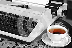 A typewriter, tea and a rose in a vase.