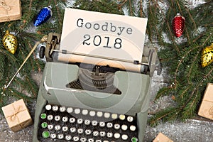 Typewriter with text `Goodbye 2018`, spruce branches and gift boxes on a wooden table