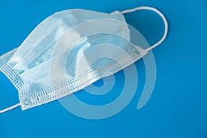 A typical 3-layer medical surgical mask to cover the mouth and nose on a blue background.