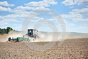 Typical agricultural scene tractor cultivation in field in clouds of dust drives off into the distance. Selective focus