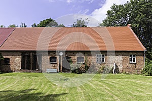 A typical barn with red brick walls and modern red roof surrounded with gr