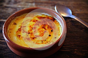 Typical `crema catalana` served on a clay plate on a rustic wooden table with a spoon.