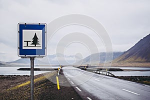 Typical dark gray wet asphalt of beautiful Icelandic roads. Highway and bridge over the lake between the bold mountains covered by photo