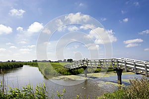 Typical Dutch landscape with green meadows, grass, bridge, water, blue sky and clouds