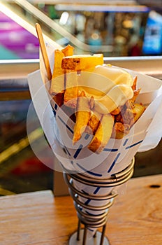 Typical Dutch street food .Hand holding traditional potato dish from Netherlands. Fried potatoes in paper cone topped with