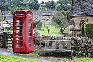 Typical English Red Telephone booth at medieval St Barnabas Anglican church with cemetery and stone wall gate in Snowshill