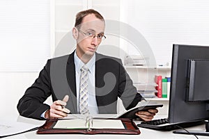 Typical examiner or controller - arrogant and disagreeable sitting at desk with computer