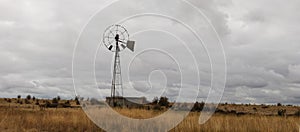 typical farming scene of an old tin wind powered water pump standing tall in an open field full of dry, drought affected grassland