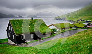 Typical Faroese village with traditional grass roof house and stunning fjord landscape on horizon. Bour Village. Vagar Island,