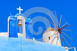 Typical Greek church tower and windmill with blue sky in background in Oia village, Santorini island, Greece