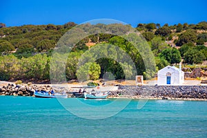 Typical Greek island view of beach, blue sea, wooden fishing boats and small white church in Istron, Crete, Greece