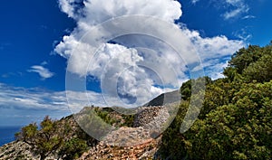 Typical Greek landscape, hill, mountain, spring foliage, bush, olive tree, rocky path. Blue sky with beautiful clouds