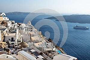Typical Greek village with church tower lying far over the ocean with cruise ship passing by, Fira, Santorini, Greece
