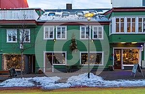 Typical Icelandic green wooden house with snow on the roof in a Reykjavik street and shops with windows with a snow covered