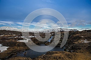 Typical Icelandic landscape: Thingvellir National Park, rivers, lava fields covered with snow against the backdrop of mountains