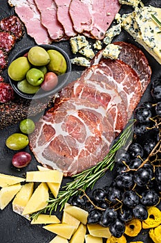 Typical italian antipasto with prosciutto, ham, cheese and olives. Black background. Top view