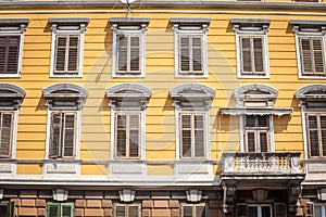 Typical italian mediterranean facade of a residential building, yellow, with traditional European wooden blinds and a balcony