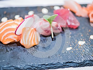 Typical Japanese dish of sushimi with tuna salmon roll on a black background