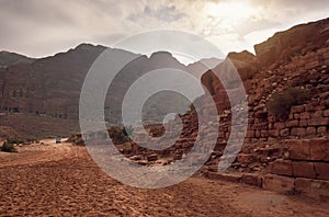 Typical landscape at Petra, Jordan, red dusty ground, mountains with carved buildings inside in distance