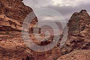 Typical landscape at Petra, Jordan, rocky walls around narrow canyon, few small bushes growing in red dusty ground