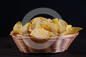 Typical mexican cuisine corn nachos, inside wicker bowl, rush isolated on black background