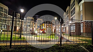 Typical modern cityscape in a new neighborhood with a playground in dark night with lanterns