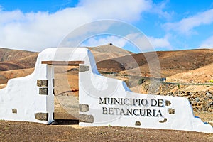 Typical municipality sign white arch gate near Betancuria village with desert mountain landscape in the background,