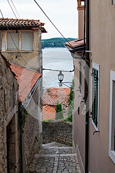Typical narrow street with steps between croatian houses with Adriatic Sea at the background in the picturesque old town of Rovinj