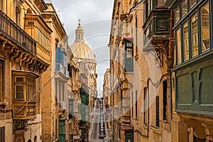 Typical narrow street of Valletta with Cathedral dome, yellow buildings and colorful balconies, Malta, Europe