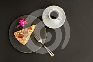 A typical Portuguese cake made of cookies on a black slate with a fork, espresso and a flower on a black background