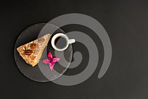 A typical Portuguese cake made of cookies called Bolo de Bolasa on a black slate with espresso and a flower on a black background.