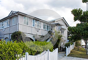 Typical Queensland house with tropical foliage and white picket fence on overcast day in Australia