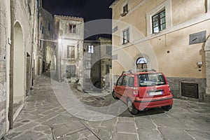 Typical red car in a narrow street in an Italian old town at night