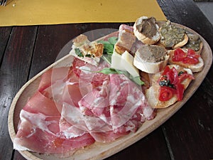 Typical rustic tuscan appetizer with crostini, prosciutto, brawn, salami, cheese on a wooden tray . Italian starter